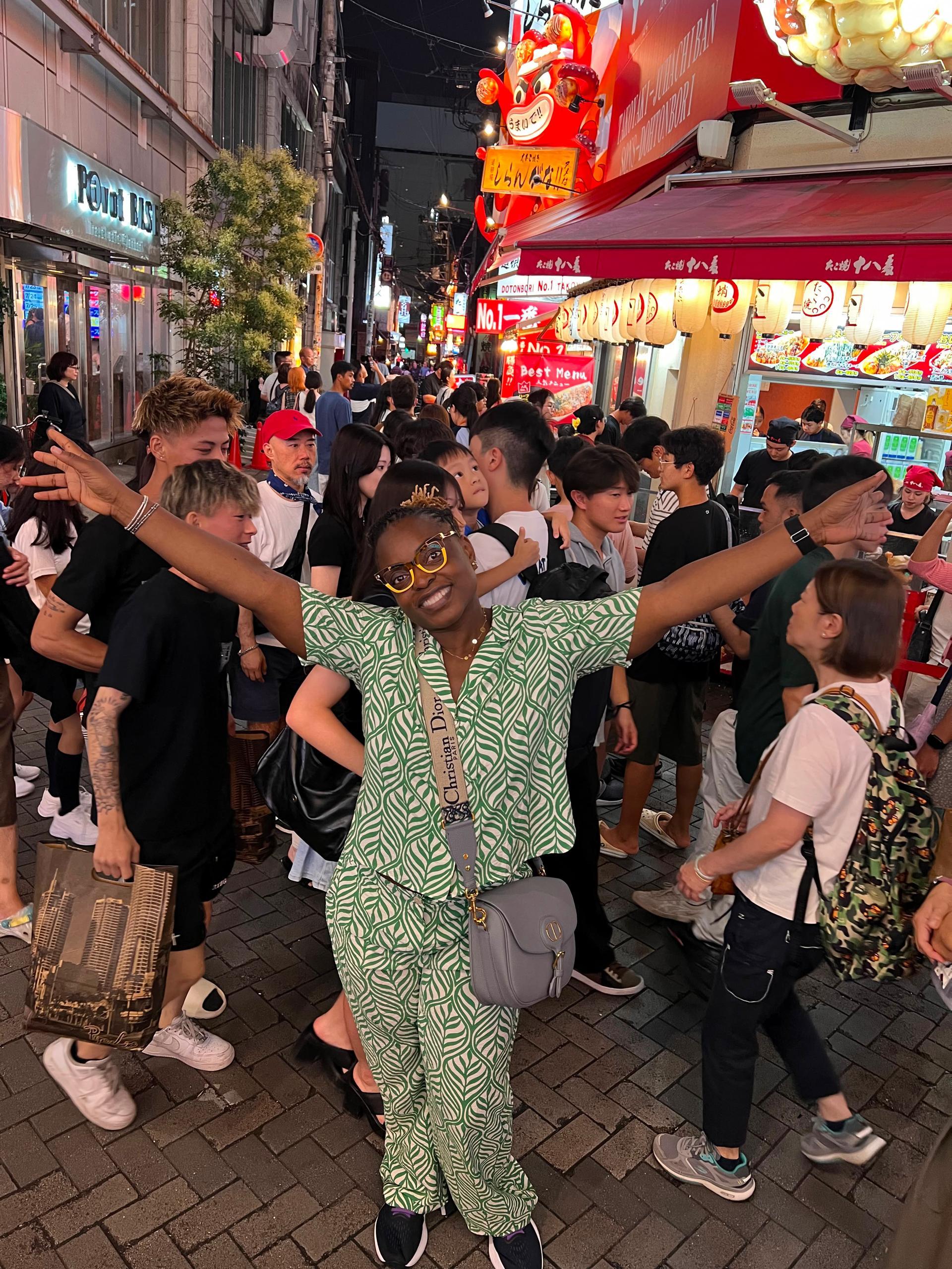 Traveler with arms outstretched on a lively night market street in Osaka, Japan