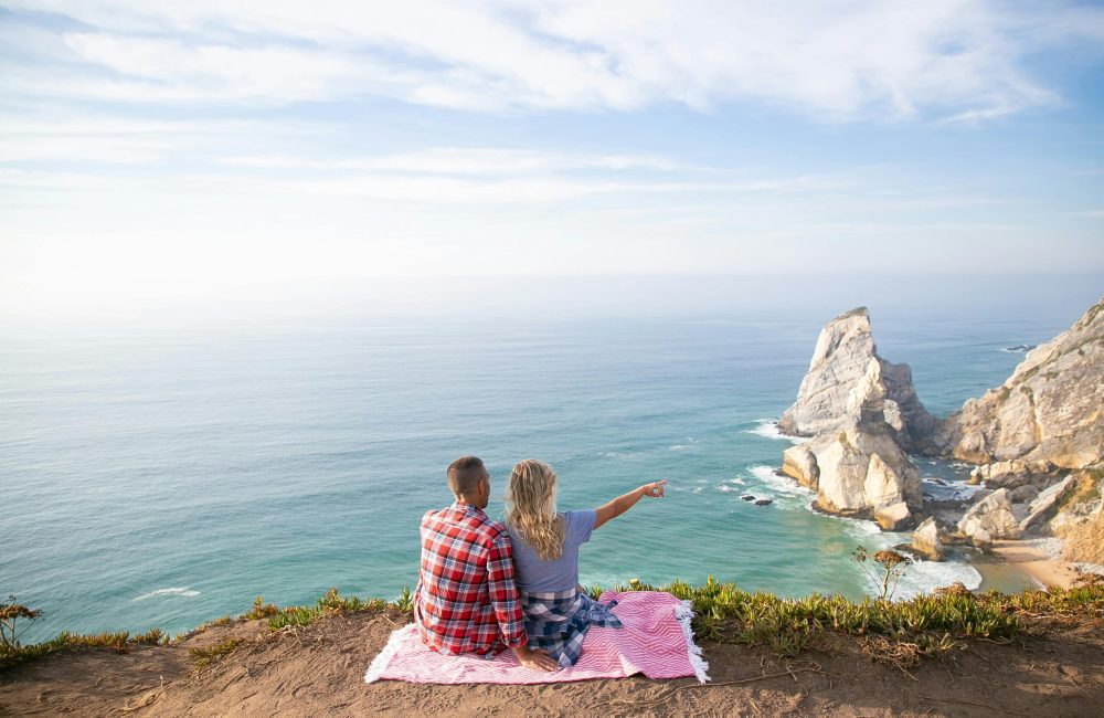 A couple enjoys a scenic view of the ocean from a cliff in Portugal. Perfect travel moment.